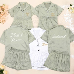 May include: Five satin pyjamas in various shades of green and white with embroidered text. The text reads "Flower Girl", "Ring Bearer", "Maid of Honour", "Bride", and "Bridesmaid".