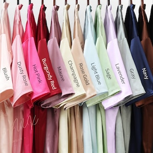 May include: A row of 15 t-shirts hanging on a clothes rail, displaying a range of colours, including white, blush, dusty rose, hot pink, burgundy red, mauve, champagne, rose gold, light blue, sage, lavender, grey, navy, brown, and black.