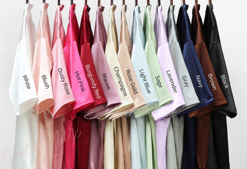May include: A row of 15 t-shirts hanging on a clothes rail, displaying a range of colours, including white, blush, dusty rose, hot pink, burgundy red, mauve, champagne, rose gold, light blue, sage, lavender, grey, navy, brown, and black.