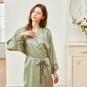 May include: A sage green satin robe with lace trim and a white embroidered name "Mavis" on the front.