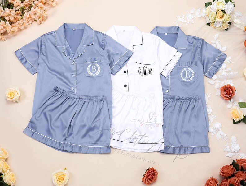 May include: Three sets of pajamas, one white and two blue. The blue pajamas have a white trim and a pocket with a white embroidered wreath and letter. The white pajamas have a black trim and the text "CMR" embroidered on the pocket.