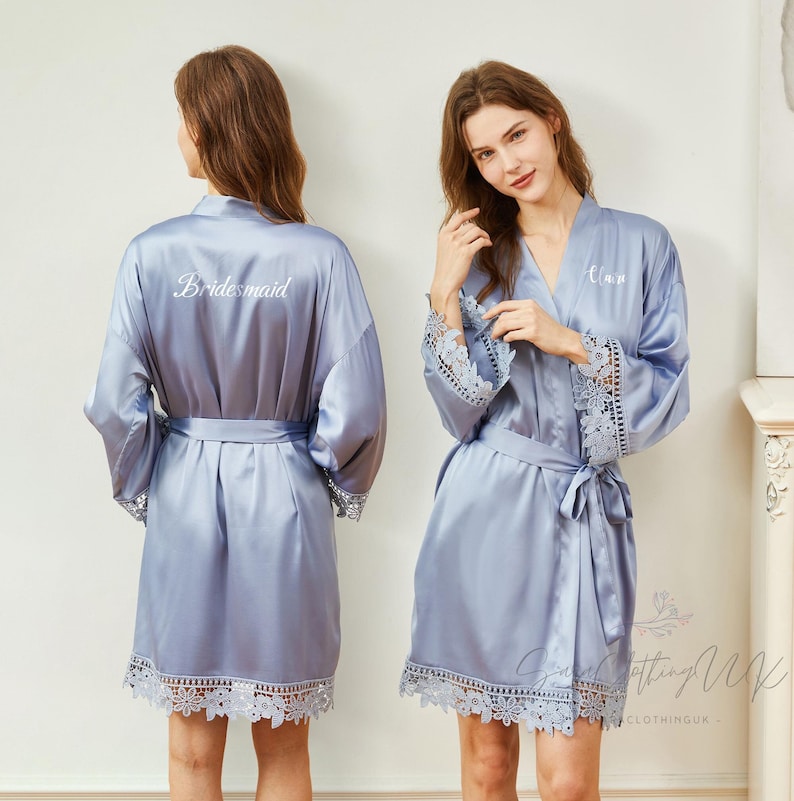 May include: A light blue satin robe with lace trim and a white embroidered inscription. The robe has a sash tie and long sleeves.
