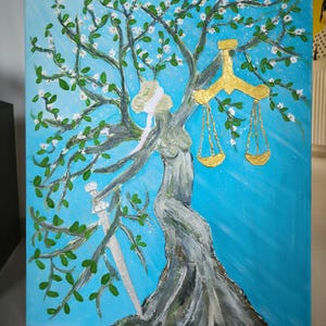 May include: An acrylic painting on canvas depicts a tree with a woman's torso and blindfold. The tree has green leaves, white blossoms, and a golden scale. A sword is visible. The background is light blue.