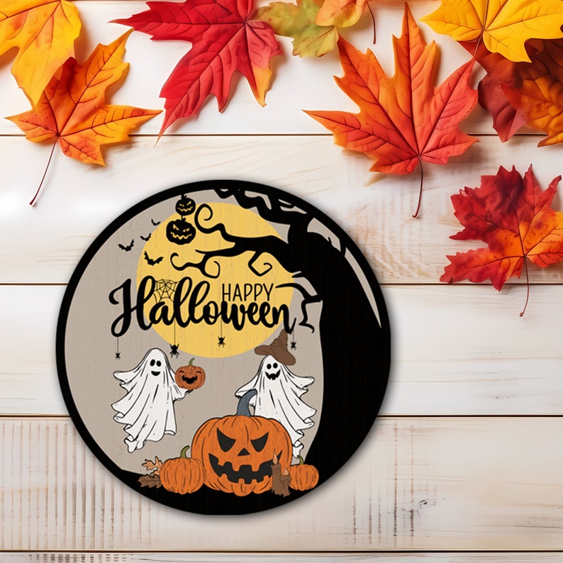 Op de afbeelding: Een ronde Halloween-bord met een grijze achtergrond, met een gele maan, een zwarte boom en de woorden "Happy Halloween". Er worden ook twee cartoongeesten en pompoenen afgebeeld. Kleurrijke herfstbladeren omringen het bord.