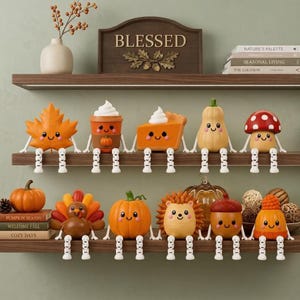 May include: A collection of ten small, decorative autumn-themed figurines with dangling white legs, including a maple leaf, pumpkin spice latte, pumpkin pie, gourd, mushroom, turkey, pumpkin, hedgehog, acorn, and a knit hat, all with smiling faces.