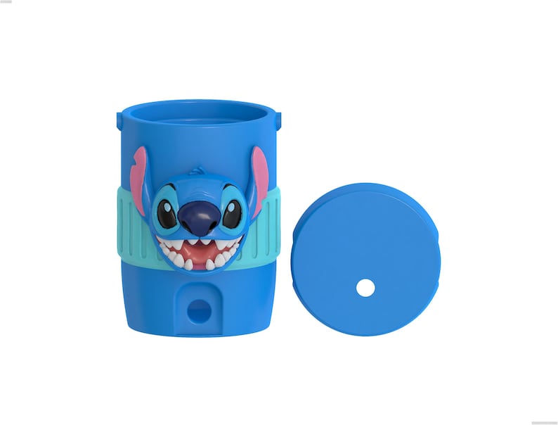 May include: A bright blue cylindrical tumbler featuring a raised, molded character face of Stitch with large ears, a dark nose, and white teeth. The cup includes a light blue textured band around the middle and a separate matching blue lid with a hole.