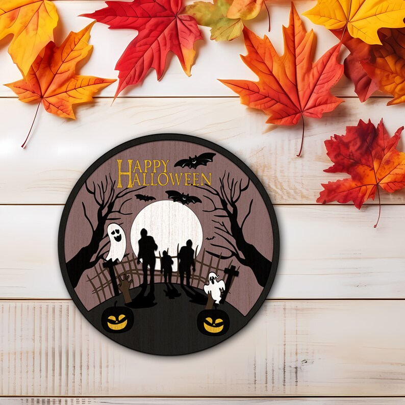 Op de afbeelding: Ronde houten Halloween-decoratie met een spookachtige sc&egrave;ne. Het ontwerp toont silhouetten van mensen, geesten, vleermuizen en pompoenen. De woorden "HAPPY HALLOWEEN" staan bovenaan. Herfstbladeren in rood, oranje en geel omringen de decoratie.