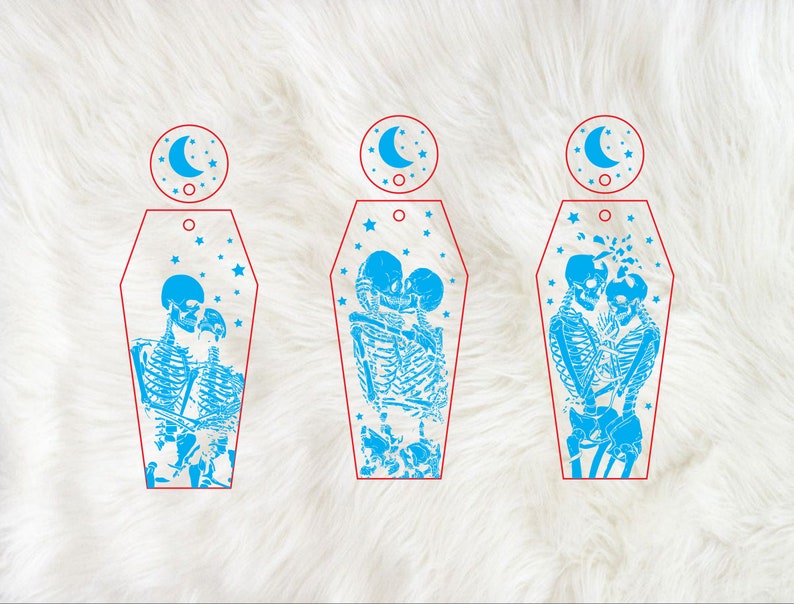 Op de afbeelding: Drie blauwe en witte kistvormige ornamenten met een skeletpaar dat elkaar kust in elk ornament. Elk ornament heeft een halve maan en sterren op de achtergrond.