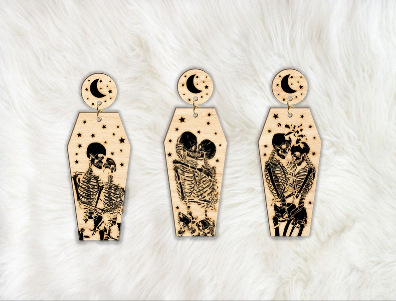 Op de afbeelding: Een paar houten oorbellen met een halve maan en een stel skeletten dat elkaar omarmt in een kist. De kist is versierd met sterren.