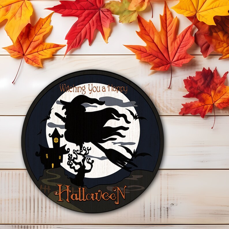 Op de afbeelding: Ronde Halloween-decoratie met een heks op een bezemsteel tegen een volle maan. Het ontwerp bevat een spookhuis en de woorden "Wishing You a Happy Halloween". Herfstbladeren in rood, oranje en geel omringen de decoratie.