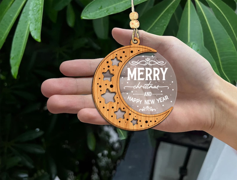 May include: A wooden crescent moon ornament with a clear acrylic insert that reads "Merry Christmas and Happy New Year". The ornament is decorated with stars and has a hole at the top for hanging.