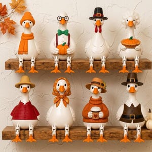 May include: Eight white goose figurines with orange beaks and feet, arranged on two wooden shelves. Each goose wears different seasonal attire, including hats, scarves, sweaters, and accessories like a pumpkin, a pie, and a coffee cup.
