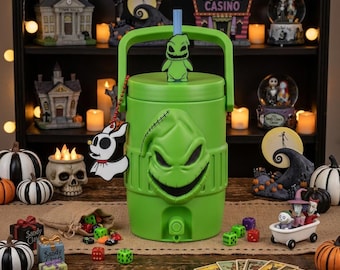 May include: A bright green beverage cooler featuring a molded Oogie Boogie face on the front, a top handle, and a blue straw. A small Oogie Boogie figure sits on the lid, and a white Zero character charm hangs from a red beaded chain on the side.