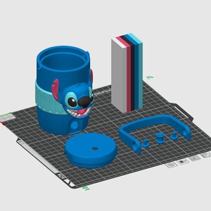 May include: A 3D digital model of a blue cylindrical container featuring a Stitch character face, a separate circular lid, a blue handle, and a rectangular block with stacked layers of white, pink, black, blue, and light blue colors.