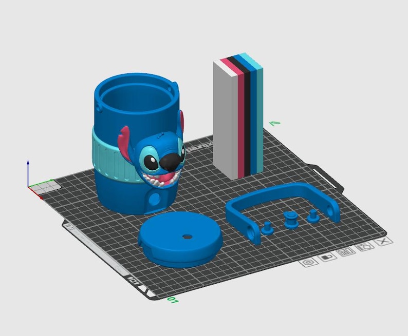 May include: A 3D digital model of a blue cylindrical container featuring a Stitch character face, a separate circular lid, a blue handle, and a rectangular block with stacked layers of white, pink, black, blue, and light blue colors.