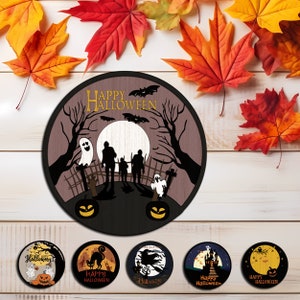 Op de afbeelding: Een ronde houten Halloween-decoratie met een spookachtige sc&egrave;ne met silhouetten van mensen, geesten, vleermuizen en pompoenen. De woorden "HAPPY HALLOWEEN" staan bovenaan. De decoratie is omgeven door kleurrijke herfstbladeren.