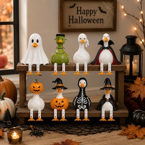 Puede incluir: Ocho figuras decorativas de patos dispuestas en un estante de madera de dos niveles, cada una vestida con diferentes disfraces de Halloween, incluyendo un fantasma, Frankenstein, momia, vampiro, calabaza, bruja y esqueleto, con pies naranjas colgantes.