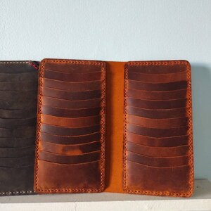May include: A brown leather card holder with multiple slots for cards. The holder is open and shows the interior lining, which is a lighter shade of brown.