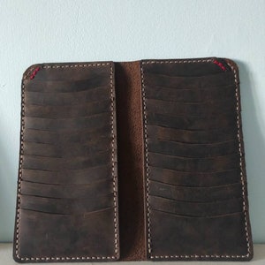 May include: A brown leather wallet with multiple card slots and a stitched edge. The wallet is closed and lying on a white surface.