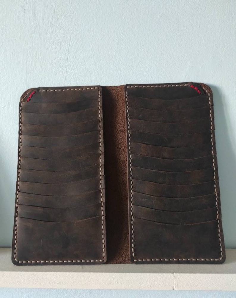 May include: A brown leather wallet with multiple card slots and a stitched edge. The wallet is closed and lying on a white surface.