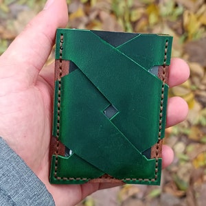 May include: A green leather wallet with a brown leather trim and a woven design. The wallet is stitched with a brown thread.