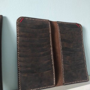 May include: A brown leather wallet with multiple card slots and a stitched edge. The wallet is closed and has a white stitching detail.