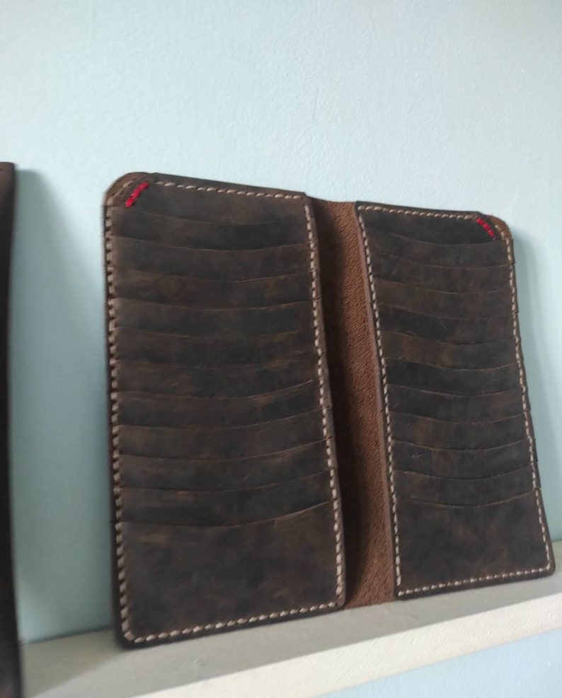 May include: A brown leather wallet with multiple card slots and a stitched edge. The wallet is closed and has a white stitching detail.