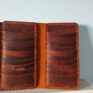 May include: A brown leather card holder with multiple slots for cards. The holder is open and the inside is a lighter shade of brown.