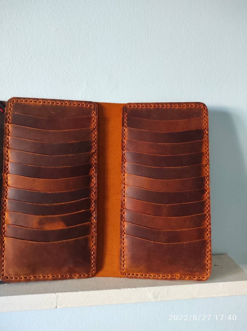 May include: A brown leather card holder with multiple slots for cards. The holder is open and the inside is a lighter shade of brown.
