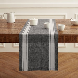 May include: A gray table runner with white stripes down the sides is displayed on a wooden table. White ceramic serving pieces, including a pitcher, sugar bowl, and small bowls, are arranged on the table.