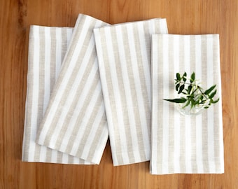 May include: Four beige linen napkins with white stripes. The napkins are folded and arranged on a wooden surface.