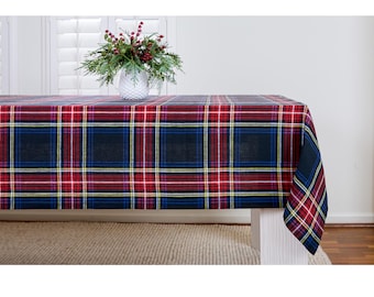 May include: A rectangular plaid tablecloth in red, navy blue, white, and yellow. The tablecloth is draped over a white table. A white vase with greenery and red berries sits on the table.