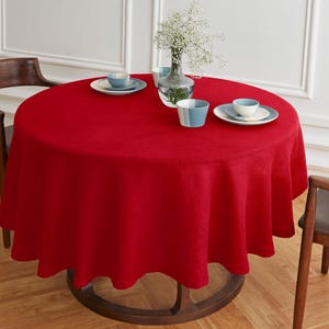 May include: A red round tablecloth with a smooth texture, covering a wooden table with a round top.  There are three blue and white ceramic dishes and a vase with white flowers on the table.