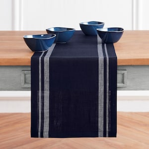 May include: A dark navy blue table runner featuring two vertical light gray stripes on each side, draped over a wooden table. Four matching dark navy blue bowls with a smooth, rounded shape are arranged on top of the runner.