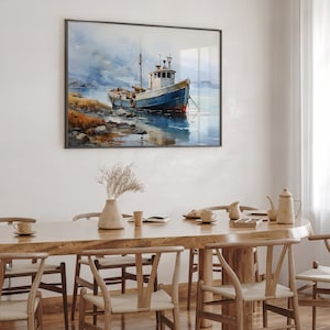 May include: A watercolour painting of a blue and white fishing boat moored in a harbour. The boat is surrounded by water and a rocky shore. The painting is framed in a black frame and hangs on a white wall above a wooden dining table with chairs.