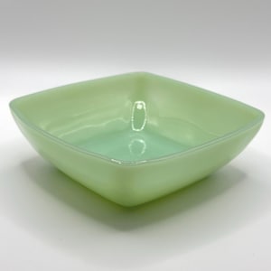 May include: A square, light green glass bowl. The bowl has a smooth, glossy finish and a slightly rounded shape. The interior of the bowl is a lighter shade of green.