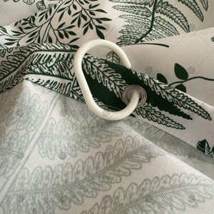 May include: White shower curtain with a green fern pattern. The curtain has a white plastic hook attached to it.