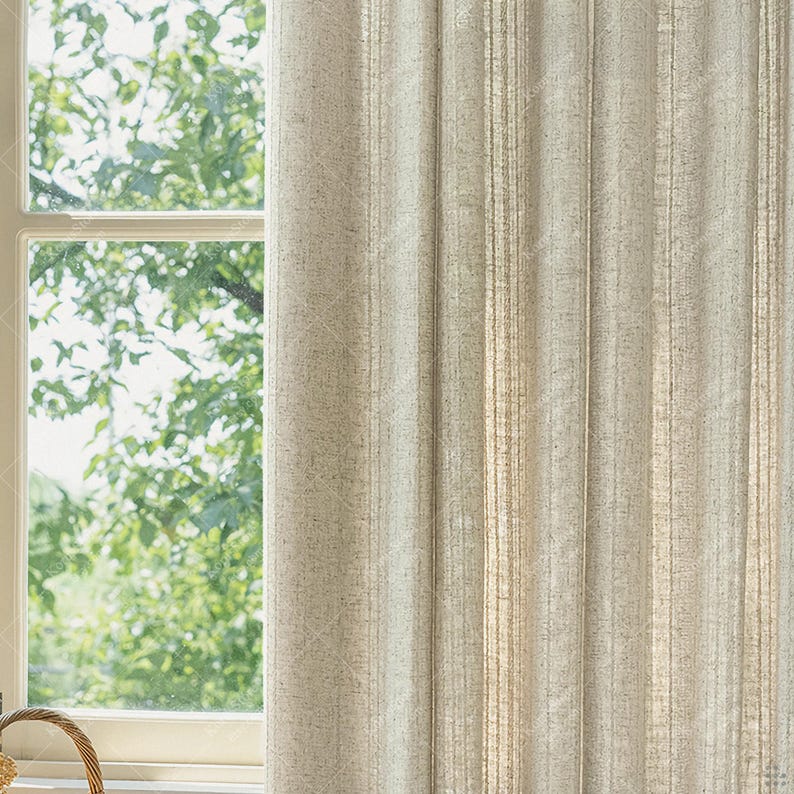 May include: Beige linen curtains hanging next to a white window frame. The curtains have vertical stripes and a textured appearance. The window reveals a view of green foliage and a wicker basket.