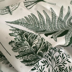 May include: White fabric with a green botanical print featuring ferns and leaves. The fabric is folded and the pattern is repeated.