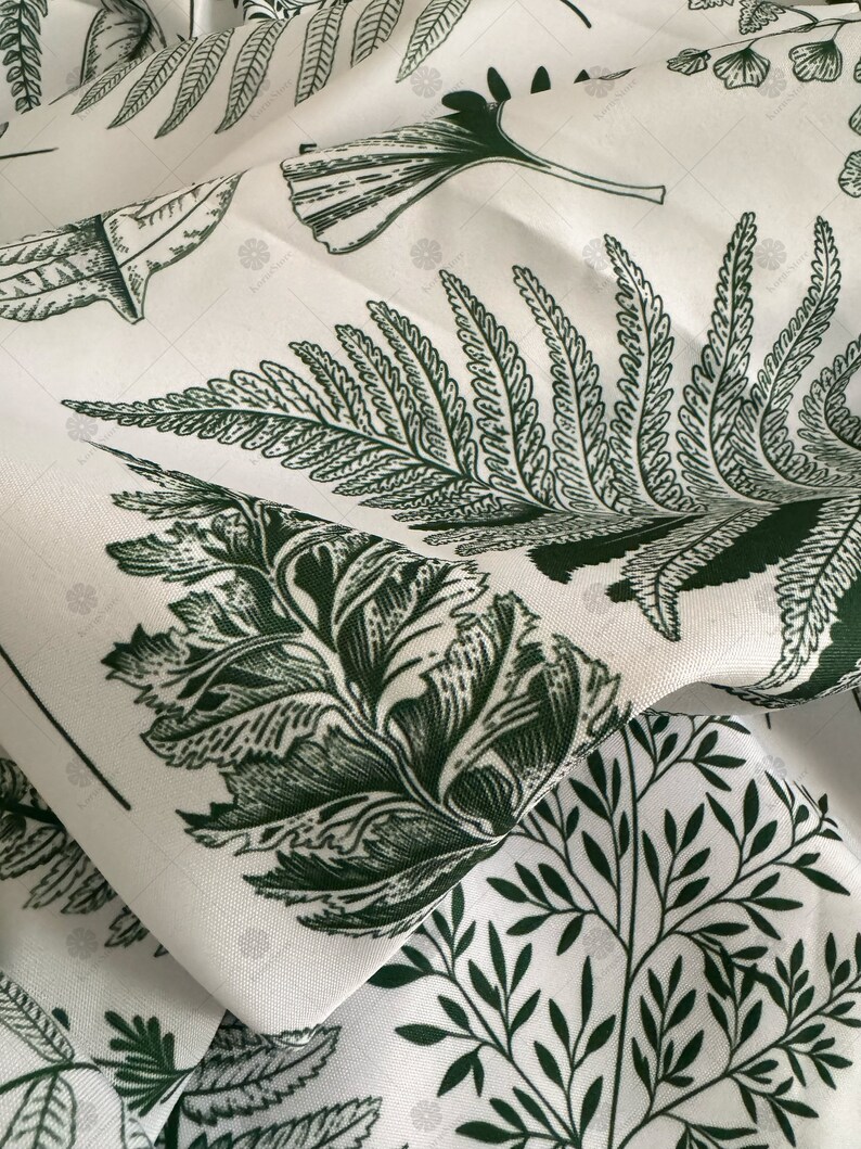 May include: White fabric with a green botanical print featuring ferns and leaves. The fabric is folded and the pattern is repeated.
