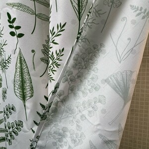 May include: White fabric shower curtain with a green and gray fern pattern. The curtain is partially open, revealing the white tiled wall behind it.