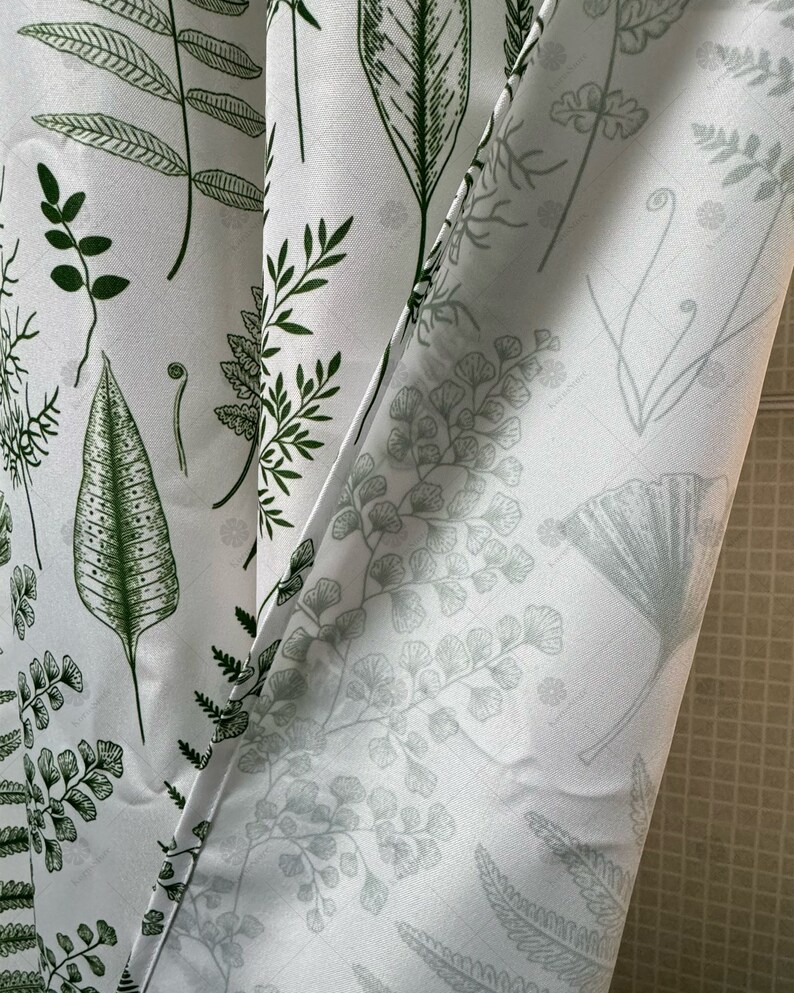 May include: White fabric shower curtain with a green and gray fern pattern. The curtain is partially open, revealing the white tiled wall behind it.