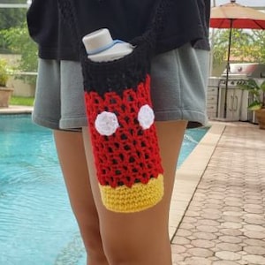 May include: A red, black, and yellow crocheted water bottle holder with white circles, resembling Mickey Mouse.