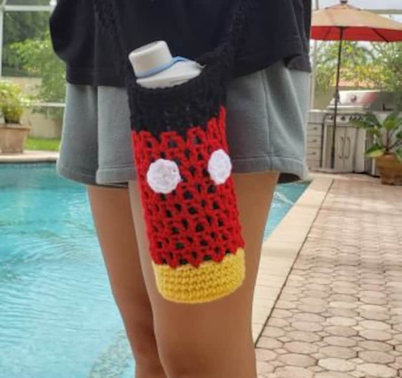 May include: A red, black, and yellow crocheted water bottle holder with white circles, resembling Mickey Mouse.