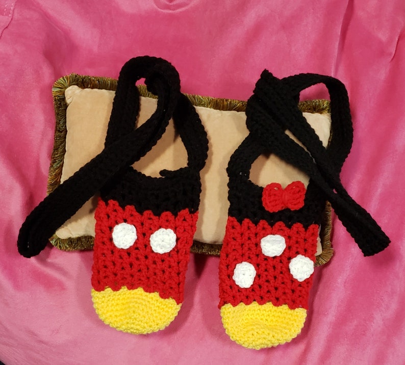 May include: A pair of crocheted Mickey Mouse slippers with black straps. The slippers are red, yellow, and white with black polka dots.