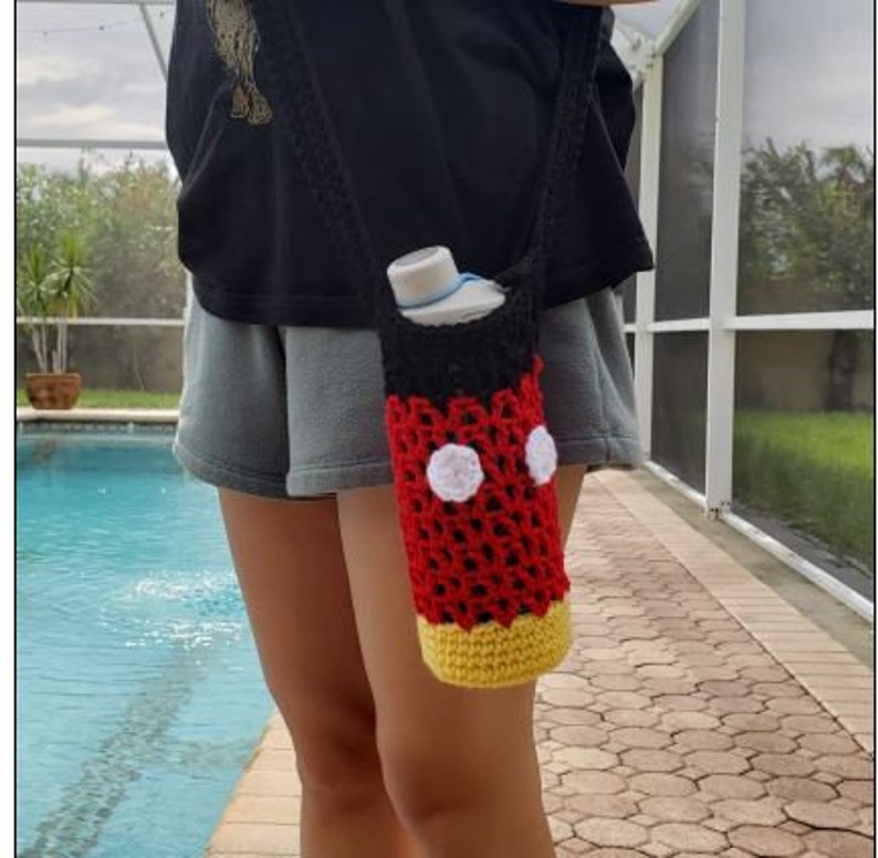May include: A red, black, and yellow crocheted water bottle holder with white circles. The holder is shaped like Mickey Mouse's head and is being worn as a crossbody bag.