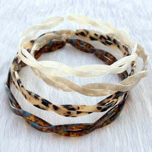 Puede incluir: Tres diademas de pl&aacute;stico trenzadas en diferentes patrones. Una es blanca, otra es marr&oacute;n con estampado de leopardo y la &uacute;ltima es marr&oacute;n con un patr&oacute;n azul y blanco.