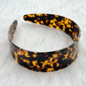 May include: A brown and black tortoiseshell headband. The headband is made of plastic and has a smooth finish.