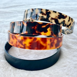 Può includere: Quattro fasce per capelli impilate in una varietà di colori e motivi. La fascia superiore ha un motivo a scaglie di tartaruga, seguita da una tartaruga marrone scuro e arancione, una tartaruga marrone chiaro e arancione e una fascia nera tinta unita in basso. Accessori moda.