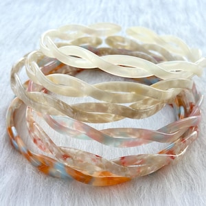 Puede incluir: Un conjunto de cuatro diademas de pl&aacute;stico trenzadas en tonos blancos, crema y melocot&oacute;n.